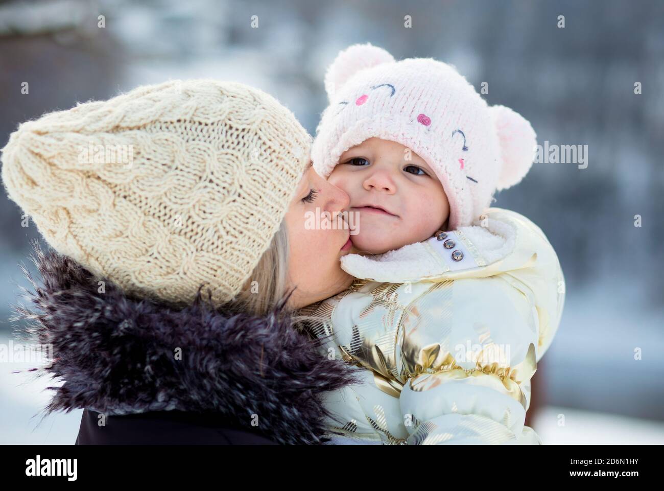 Young mom hugs her little daughter, kisses her on the cheek. Winter time, outdoor activity Stock Photo