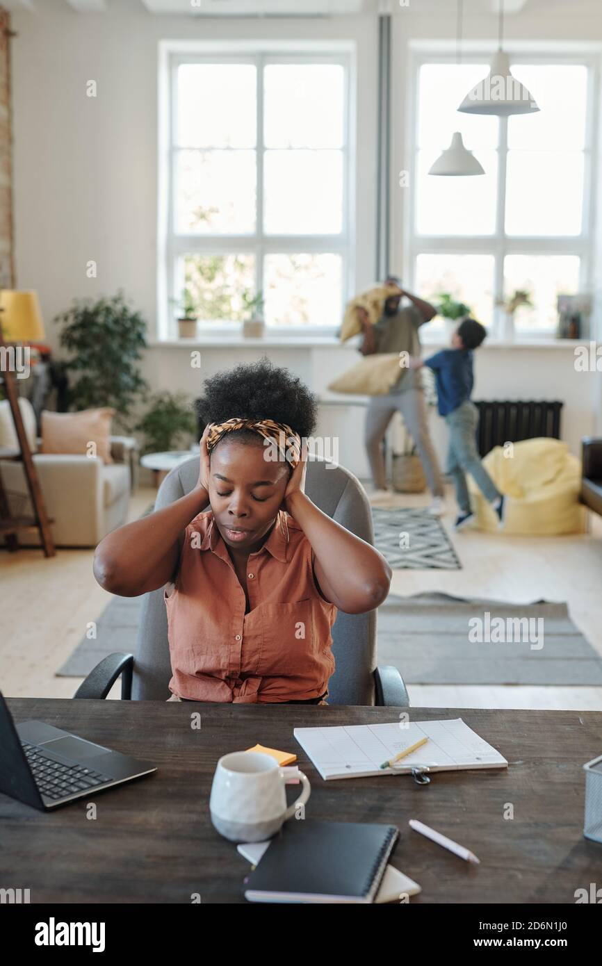 Young annoyed African woman with headache touching head while sitting by table Stock Photo