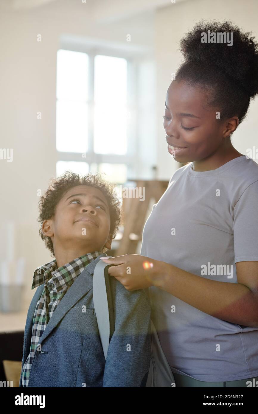 Happy young careful mother in casualwear helping her little son with backpack Stock Photo