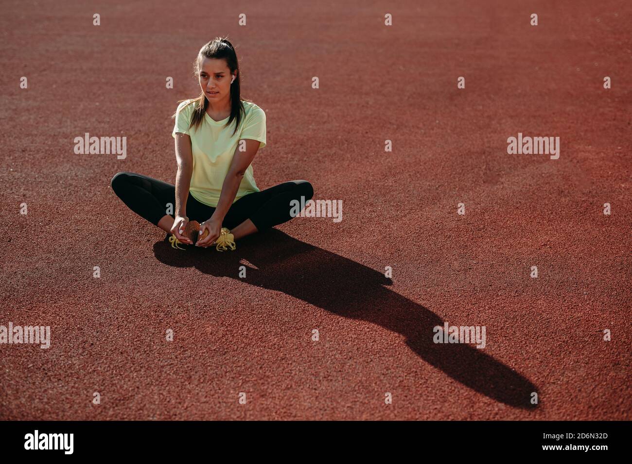 Charming brunette sitting on red court and stretching legs Stock Photo