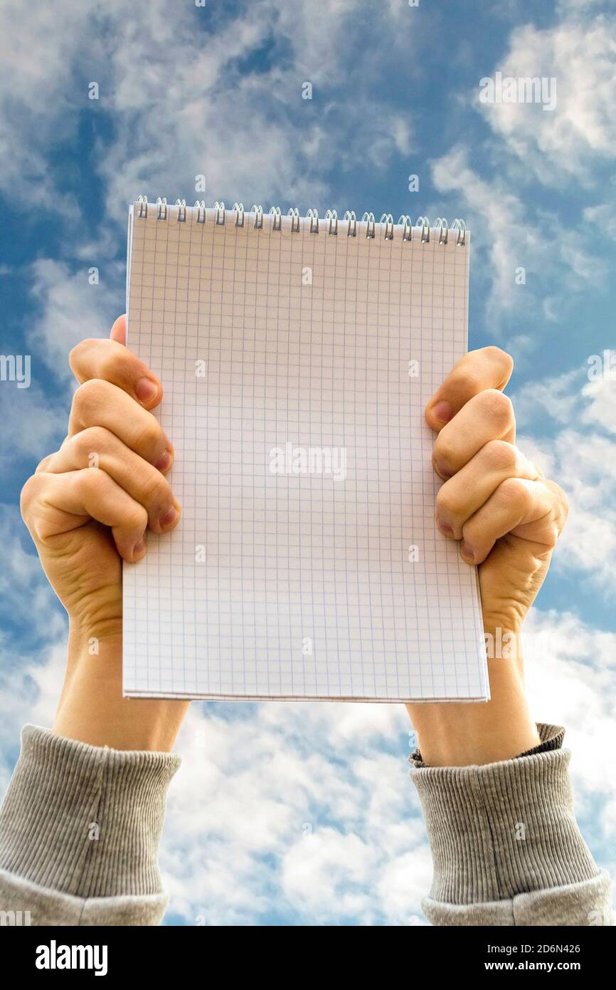 Hands holding a notebook opposite blue cloudy sky Stock Photo