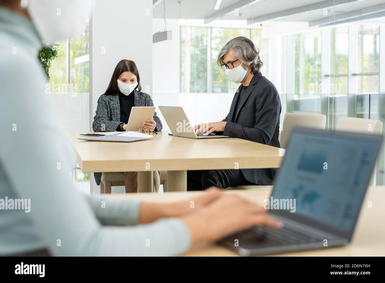 Two busy colleagues in smart casualwear and protective masks networking by table Stock Photo