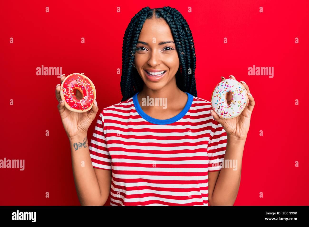 Beautiful hispanic woman holding tasty colorful doughnuts smiling with a happy and cool smile on face. showing teeth. Stock Photo