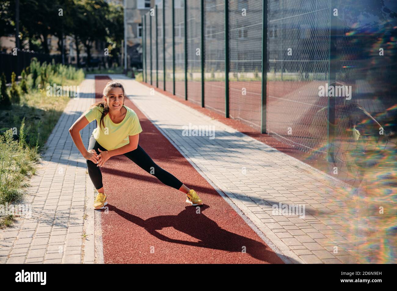 Beautiful young woman warming up on red track before run Stock Photo
