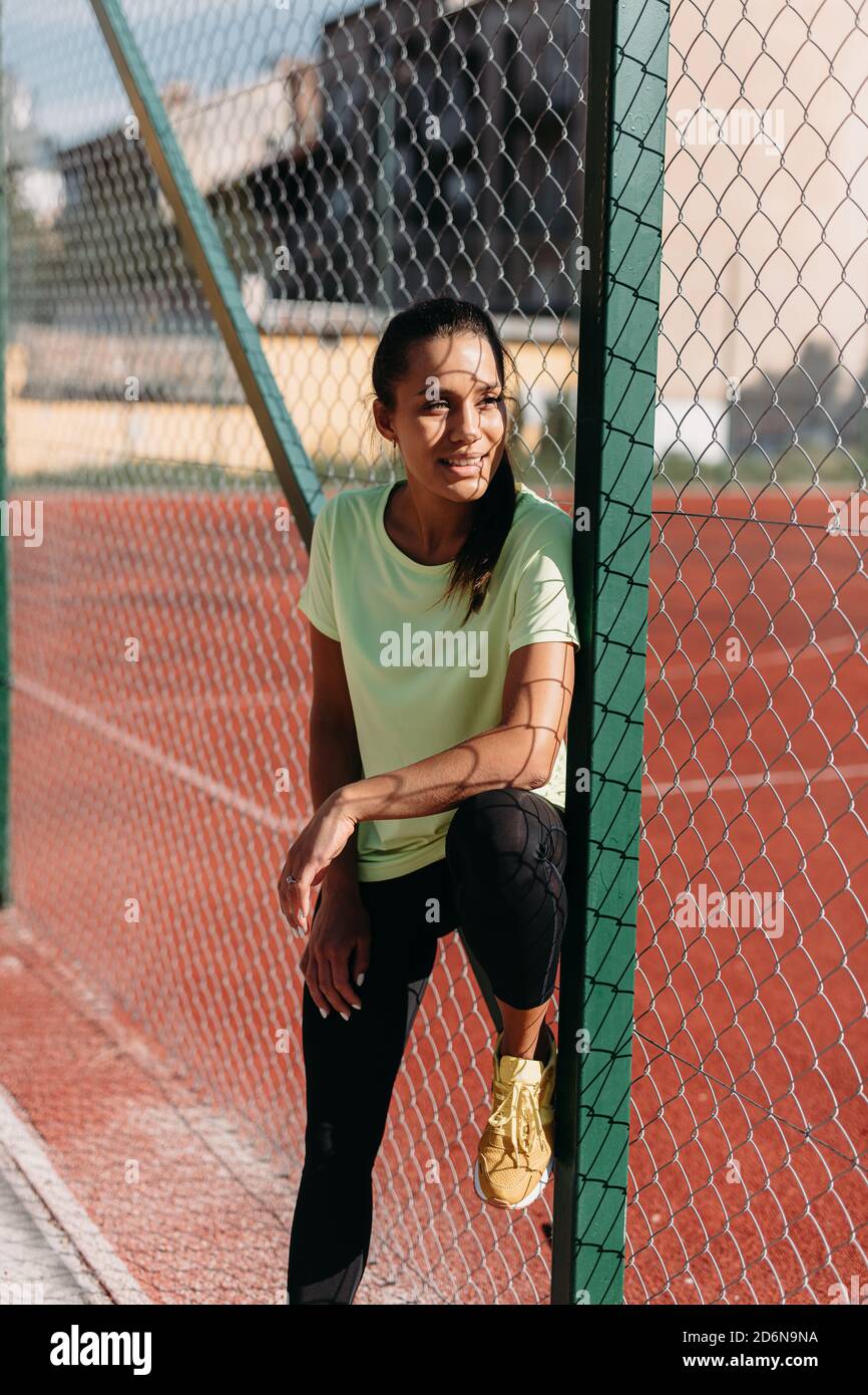 Athletic woman standing near chain link fence at stadium Stock Photo