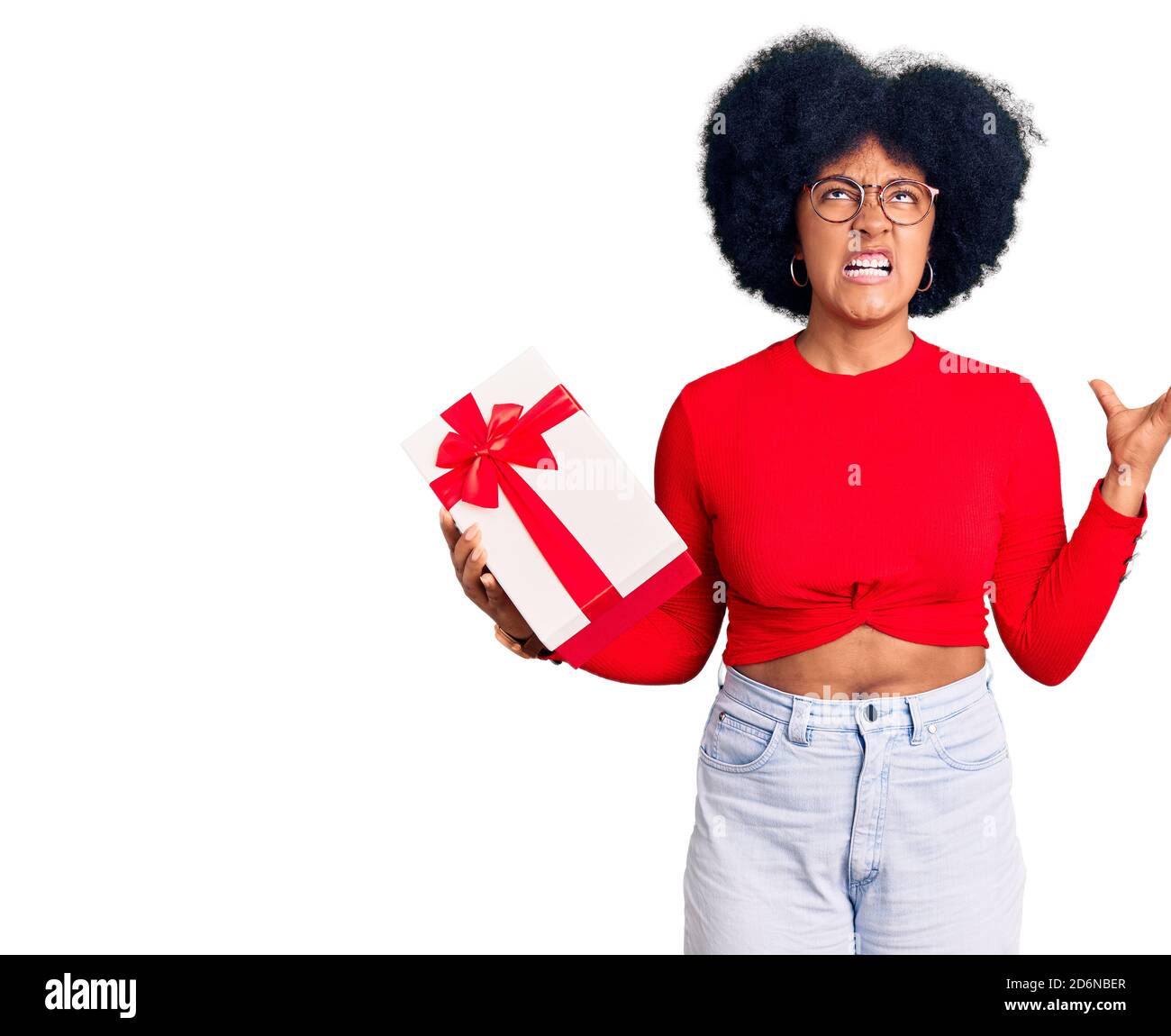 Young african american girl holding gift crazy and mad shouting and yelling with aggressive expression and arms raised. frustration concept. Stock Photo