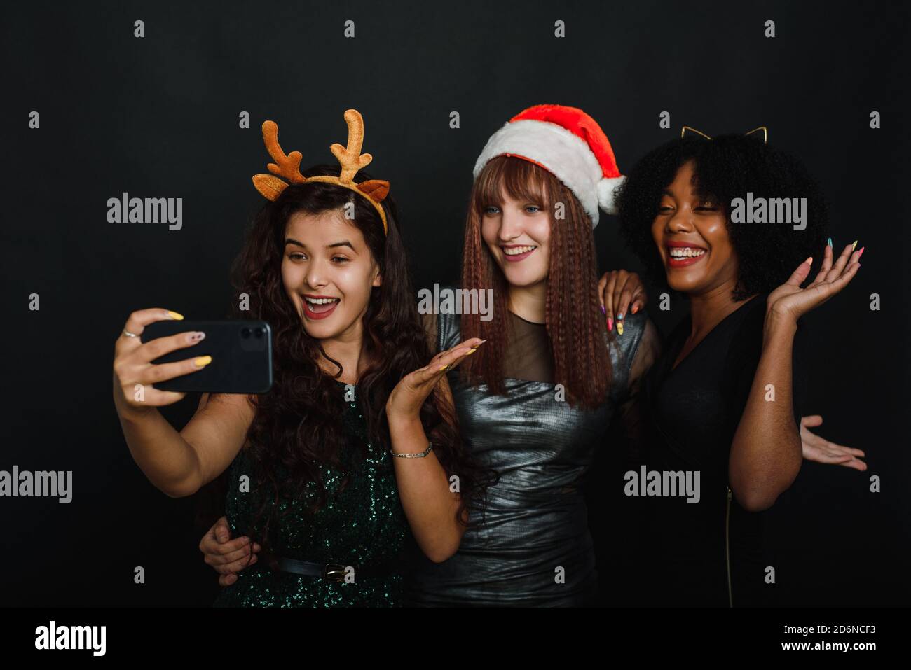 Group of friends at club making selfie and having fun. Cute young women posing with kissing face expression. Relaxed young women making selfie with friend on dark background during christmas celebration. Stock Photo