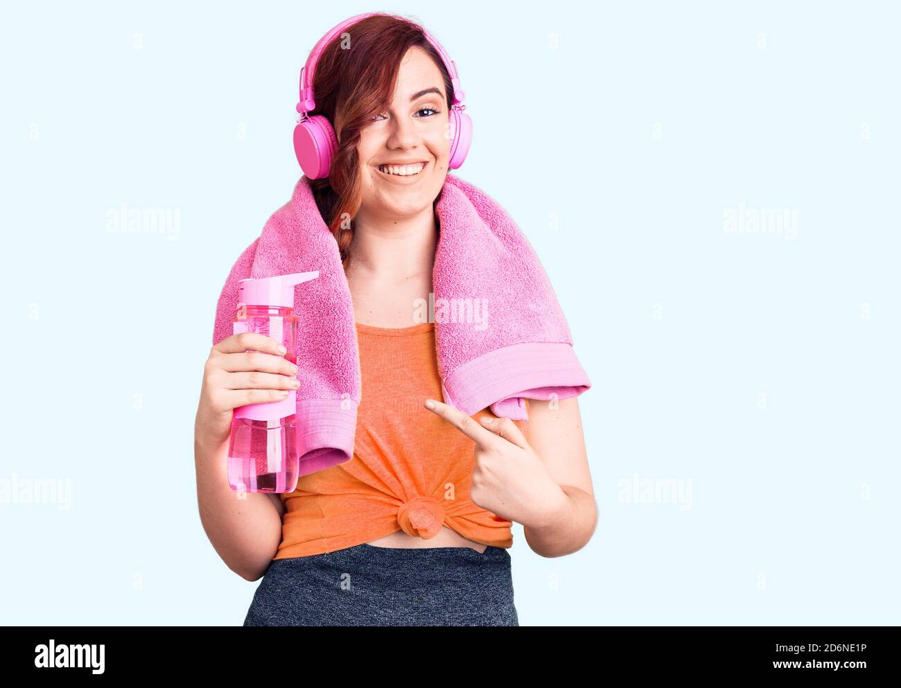 Young beautiful woman wearing sportswear and headphones holding bottle of water smiling happy pointing with hand and finger Stock Photo