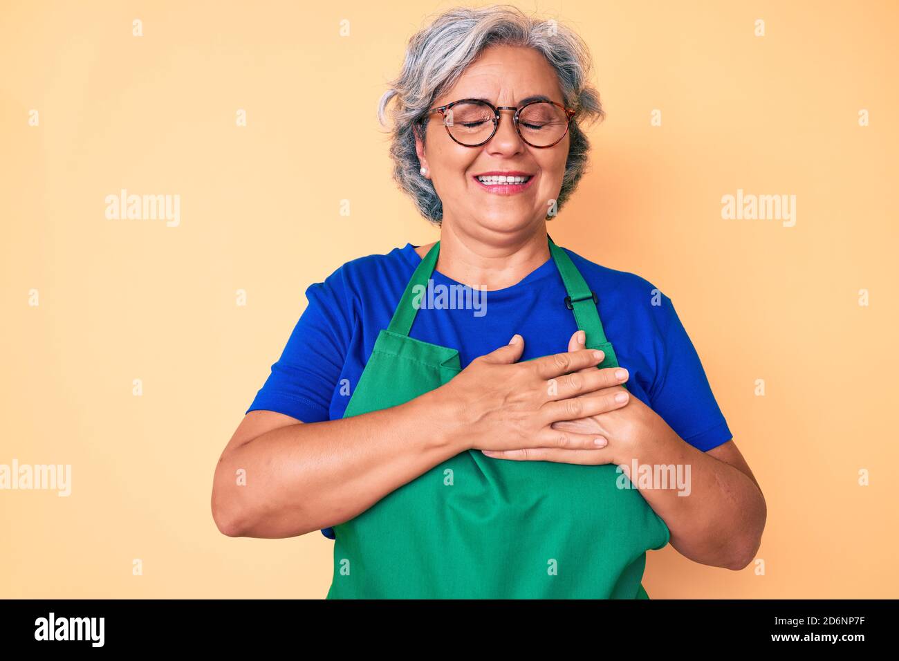 Senior hispanic woman wearing apron and glasses smiling with hands on ...
