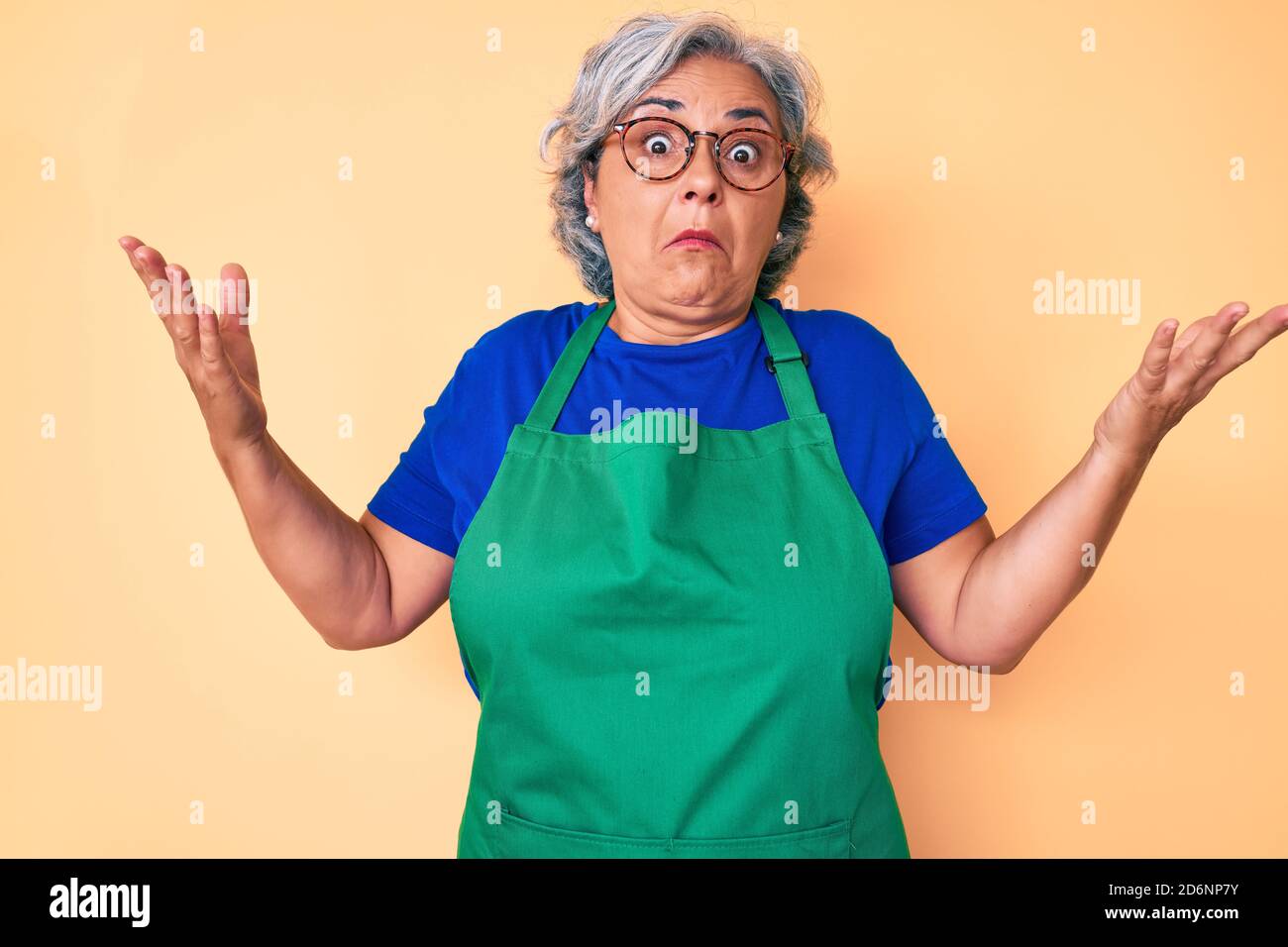 Senior hispanic woman wearing apron and glasses clueless and confused ...