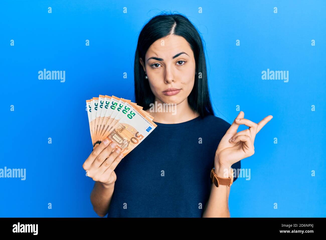 Beautiful young woman holding bunch of 50 euro banknotes pointing with hand finger to the side showing advertisement, serious and calm face Stock Photo