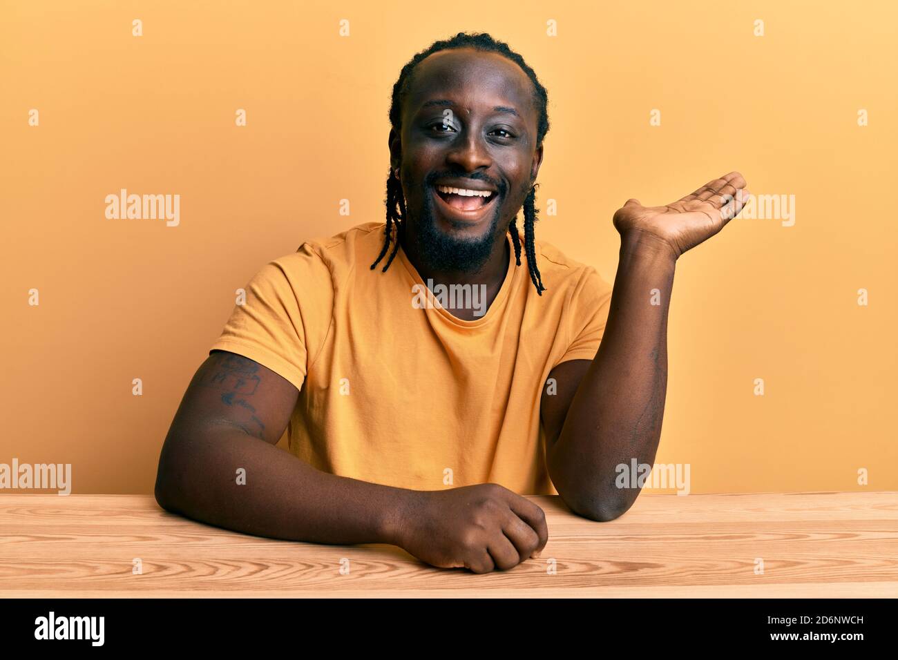 Handsome young black man wearing casual clothes sitting on the table ...