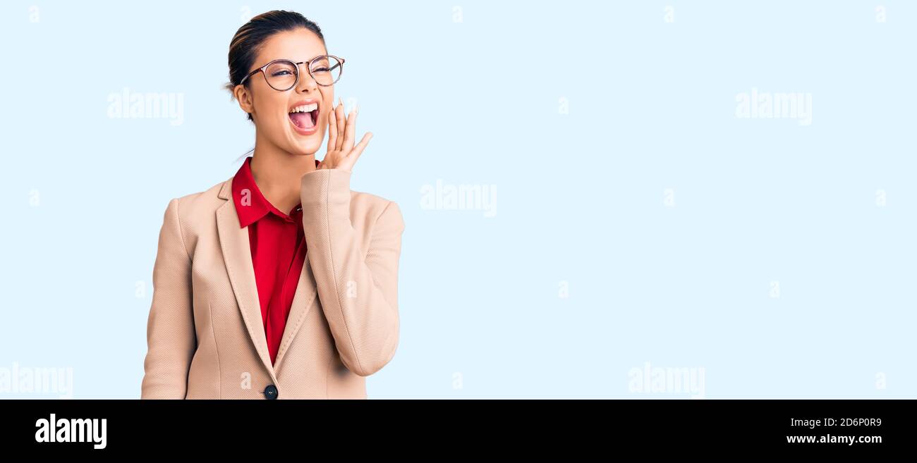 Young beautiful woman wearing business shirt and glasses shouting and ...