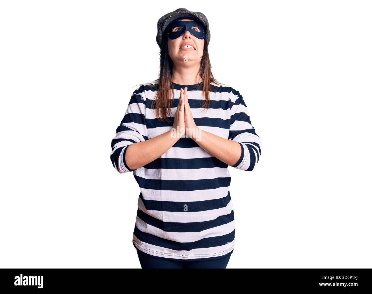 Young beautiful brunette woman wearing burglar mask begging and praying ...