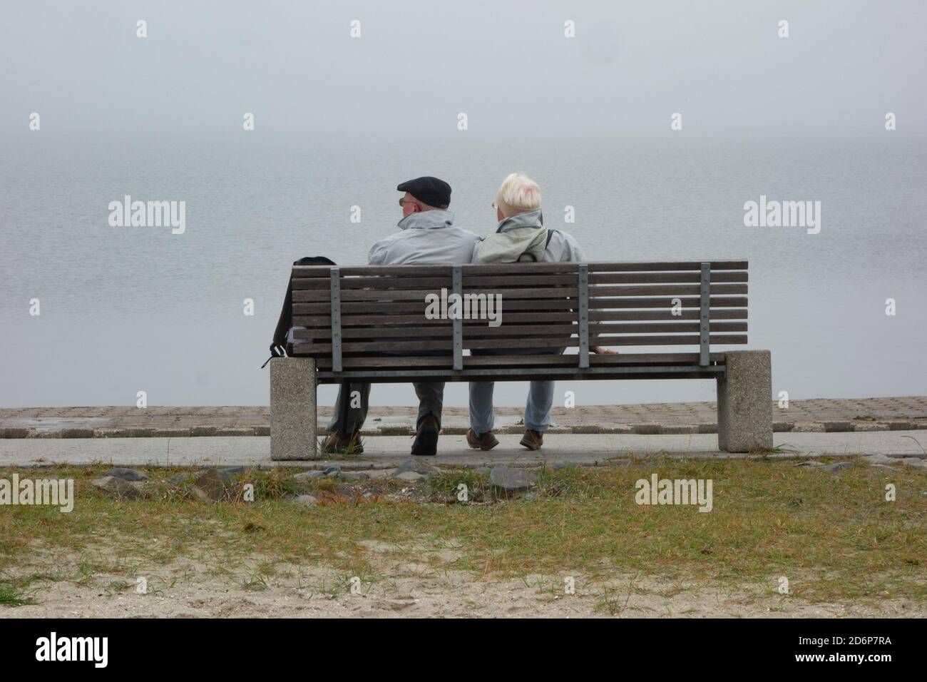 Old couple sitting on bench by the Wadden Sea. Lower Saxony. Germany. Stock Photo