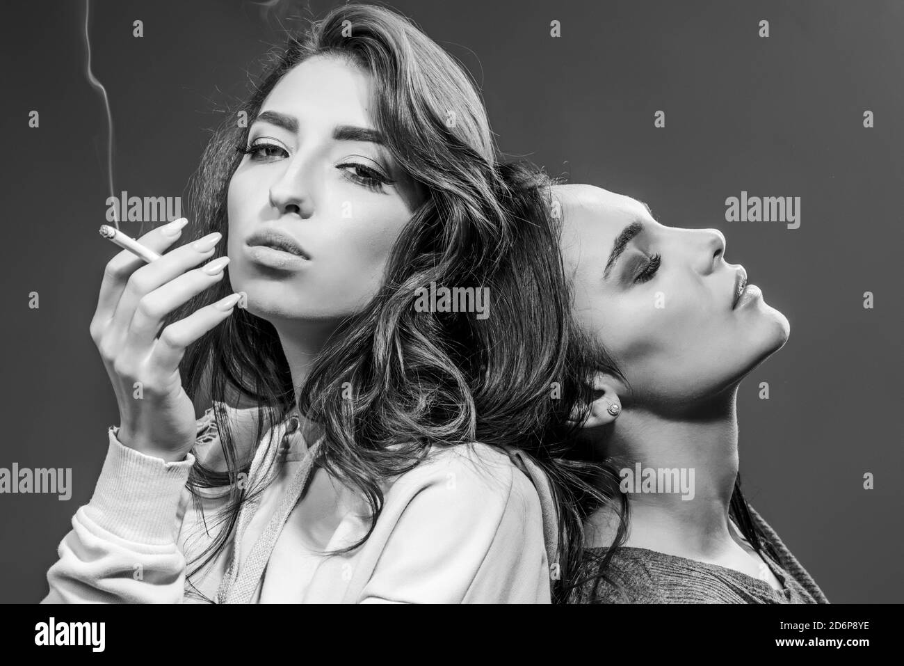 Smoking addiction. Actual social problem. Drug addict or medical abuse concept. Two sad woman with depression Smoking on the gray Background. Stock Photo