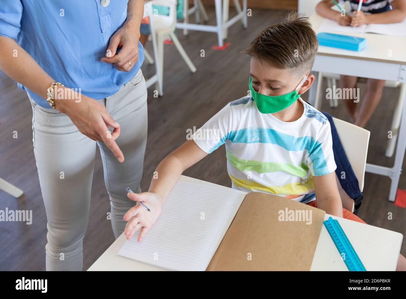 Mid section of female teacher wearing face mask teaching a boy in class