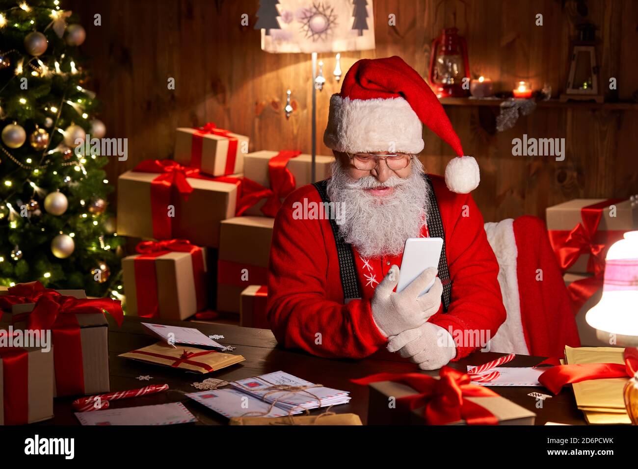 Happy Santa Claus using smartphone sitting at home table late on Christmas. Stock Photo