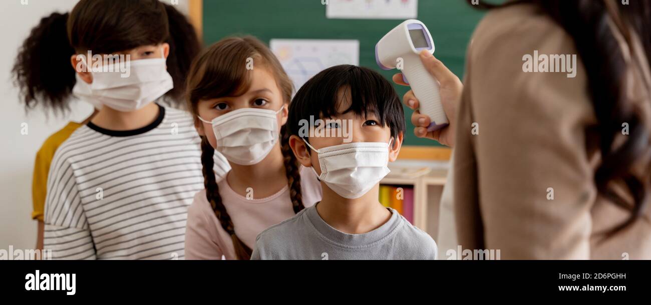 Banner group of diverse students in school building checked and scanned for temperature check. Elementary pupils are wearing face mask, line up before entering into classroom. Covid-19 school reopen Stock Photo