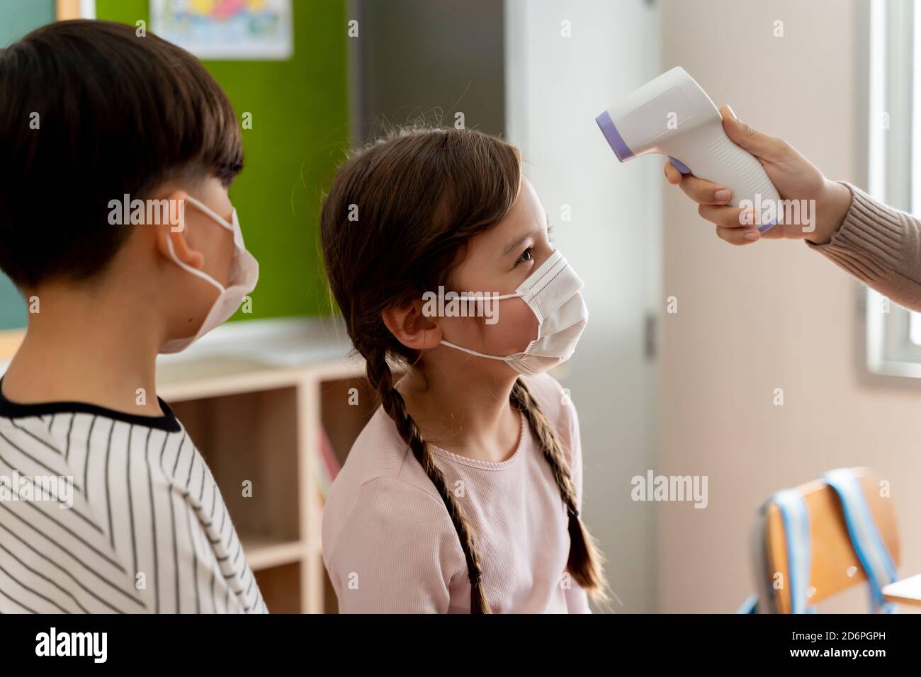 Group of Caucasian students in school building checked and scanned for temperature check. Elementary pupils are wearing a face mask and line up before entering into classroom. Covid-19 school reopen Stock Photo