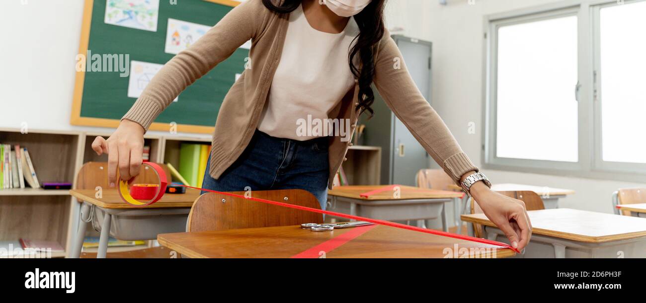 Banner of female teacher using a red tape on the desks in classroom in