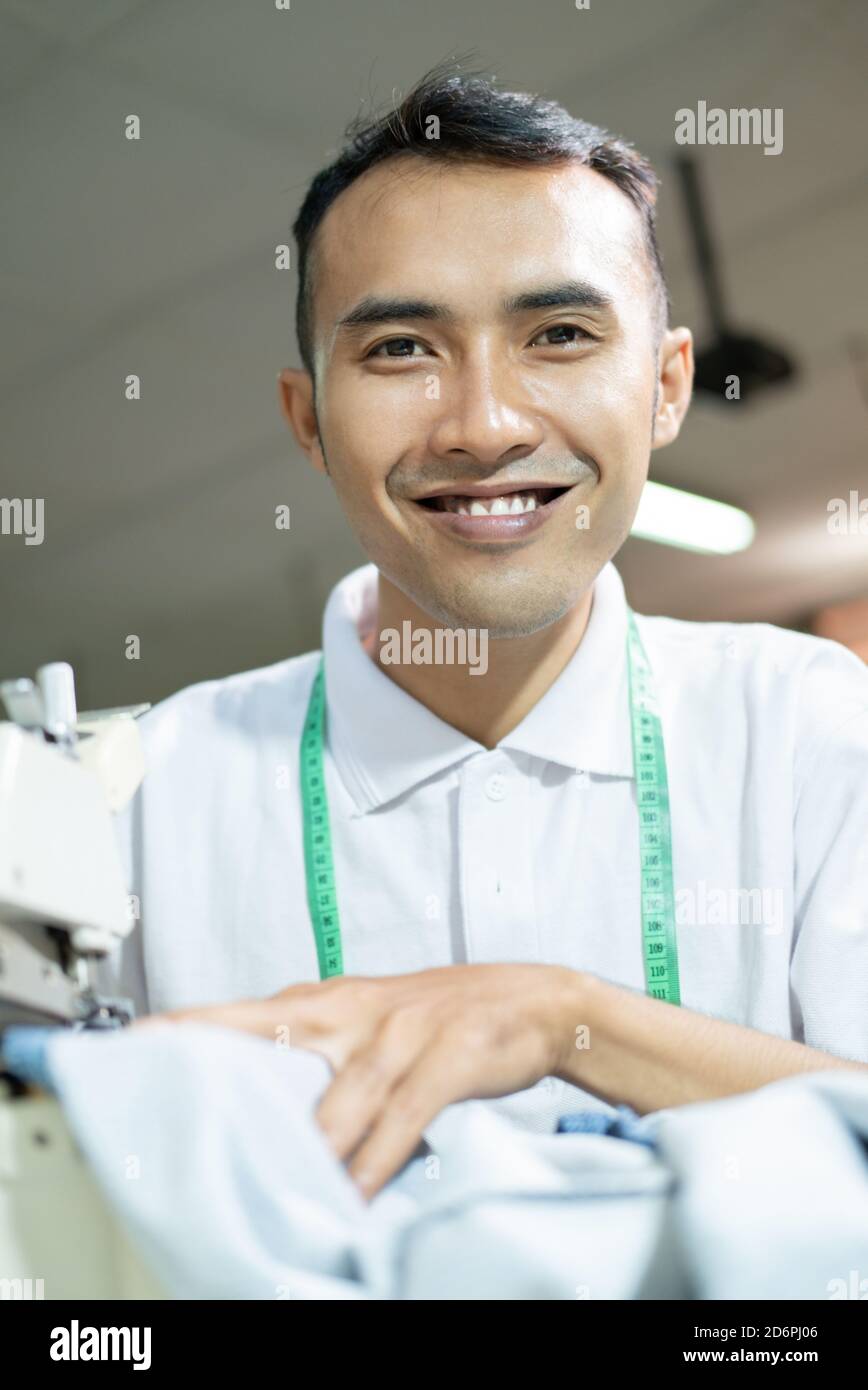 male tailor smiles looking at the camera while sewing with a sewing