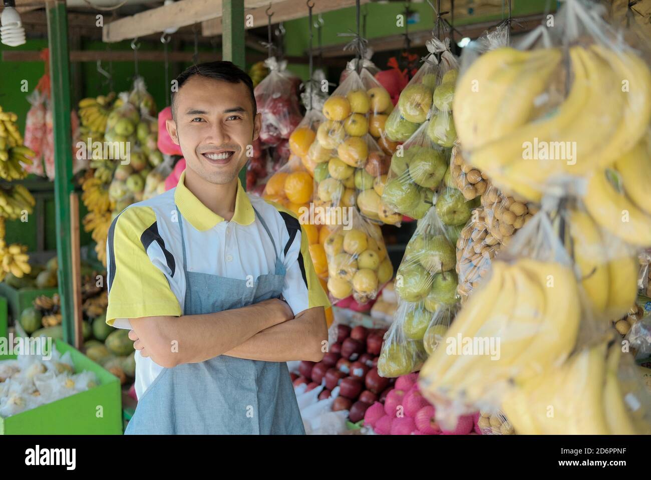 Waist up portrait of handsome young man working in fruits shop and smiling at camera while