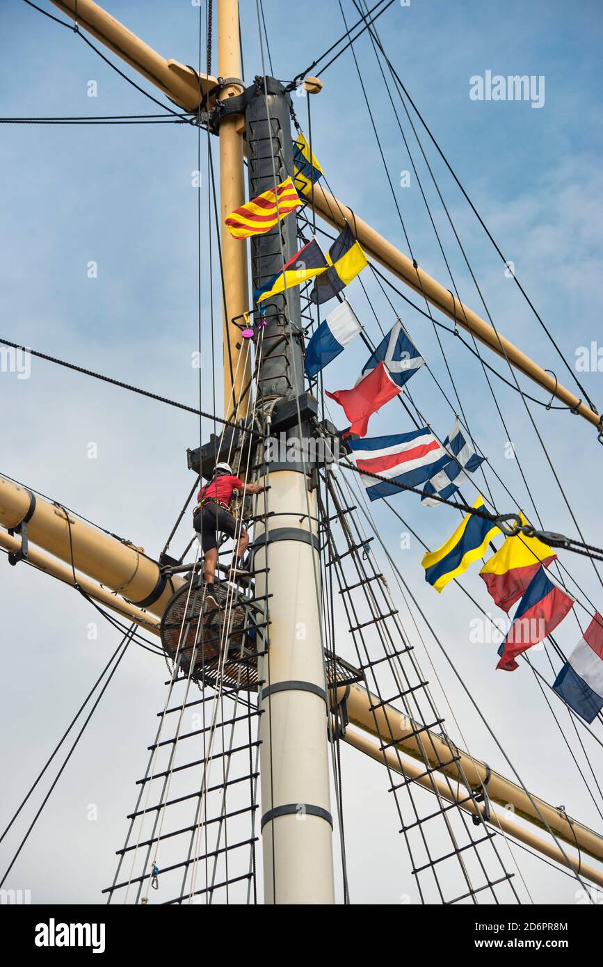 Go Aloft! SS Great Britain tourist attraction. A man is nearing the top viewing platform, climbing rigging on the mainmast on a sunny blue sky day. Stock Photo