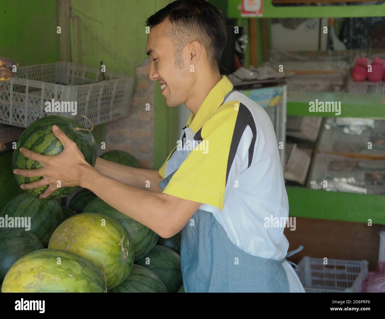 Shop attendant man in apron brings watermelon and arranges a display at ...