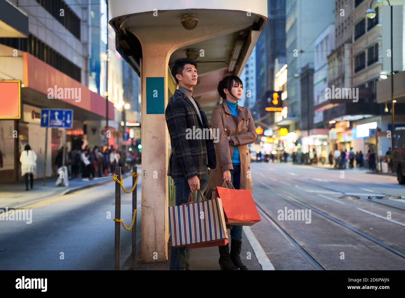beautiful young asian couple waiting for bus in modern city after shopping Stock Photo
