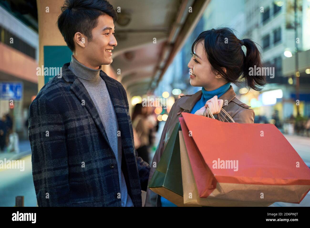 happy and loving young asian couple standing in bus station with shopping bags in hand Stock Photo