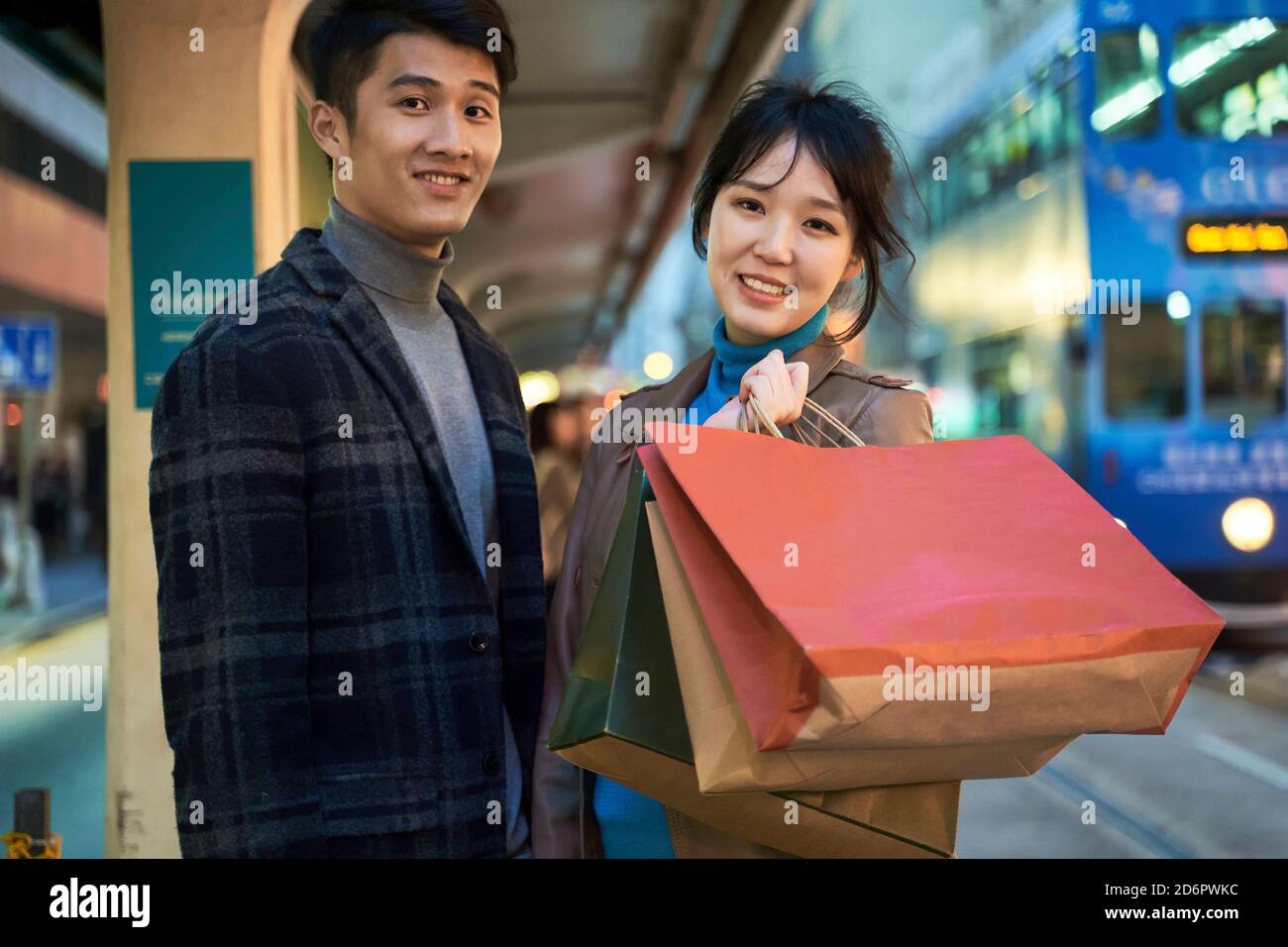 happy and loving young asian couple standing in bus station with shopping bags in hand Stock Photo