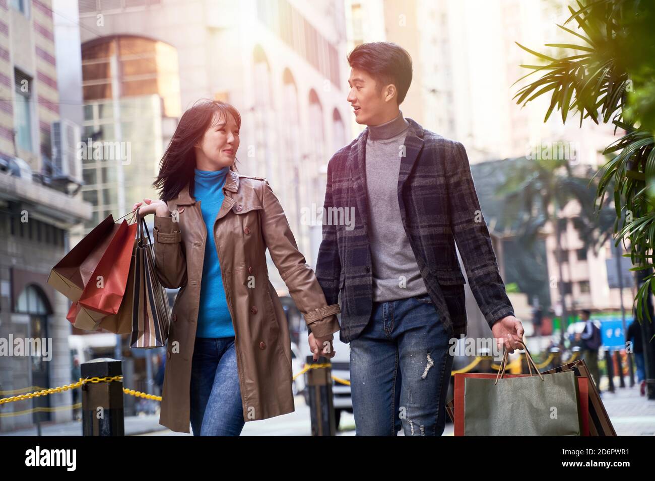 happy and loving young asian couple walking on street with shopping bags in hand Stock Photo