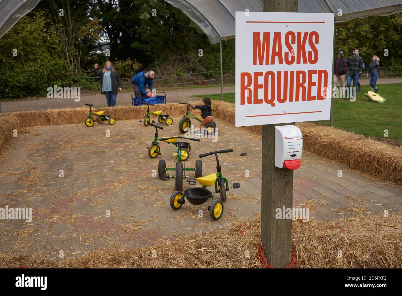 Masks required sign and hand sanitizer dispenser in a kids play area at Fir Point Farm's annual harvest festival during a pandemic fall season. Stock Photo