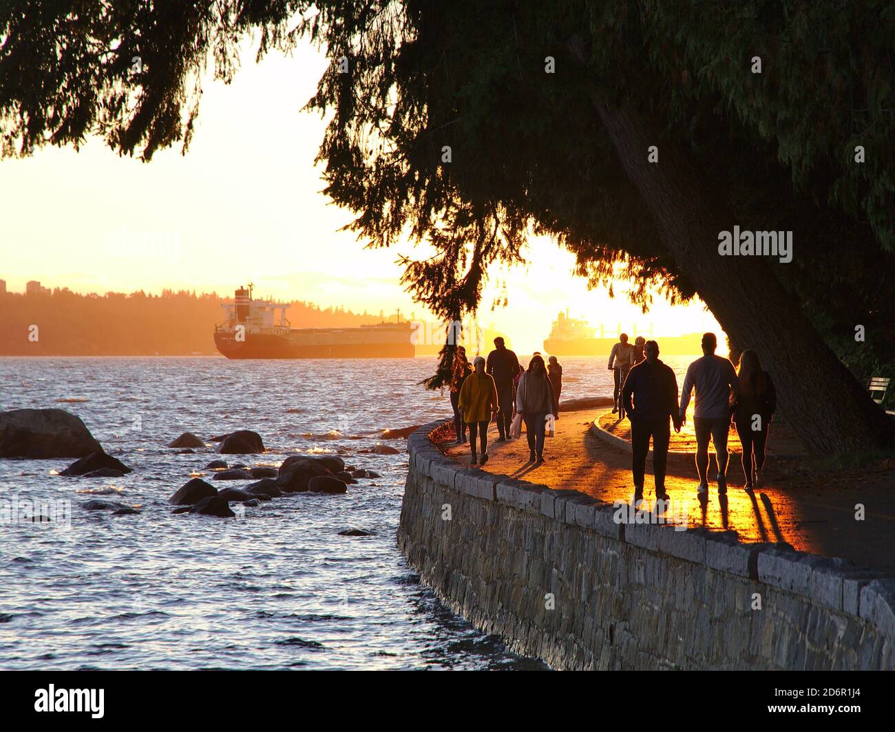 October 2020, Vancouver, Canada - People walking, running and jogging along the Stanley Park seawall. Anchored ships visible in the background. Stock Photo