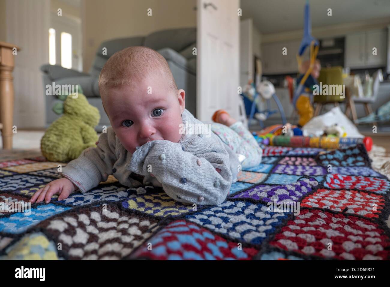 Baby girl laying on a colourful rug at home. Photo by Sam Mellish Stock Photo