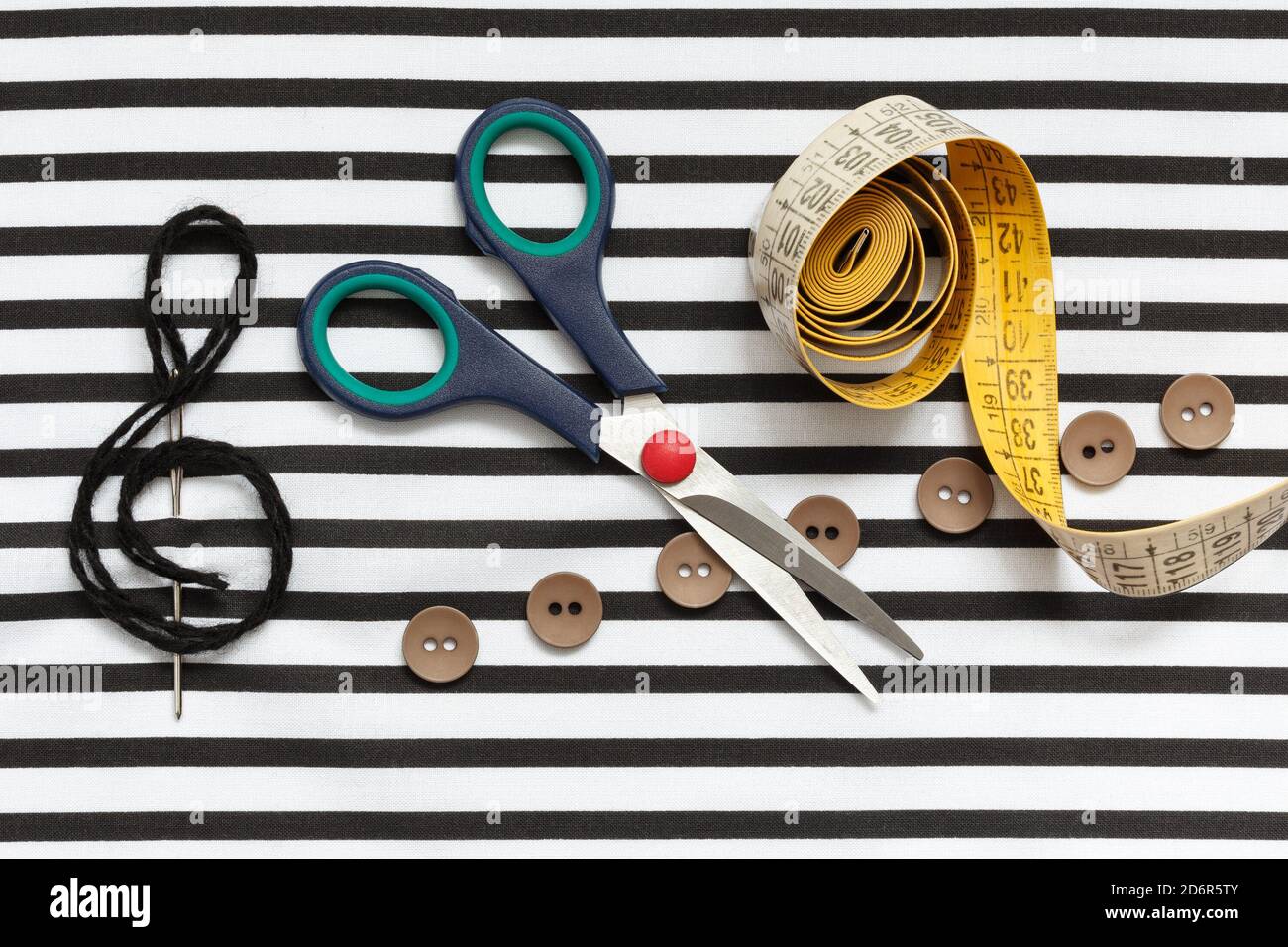 Scissors, measuring tape, needle, threads and buttons in the form of notes on striped fabric. Stock Photo