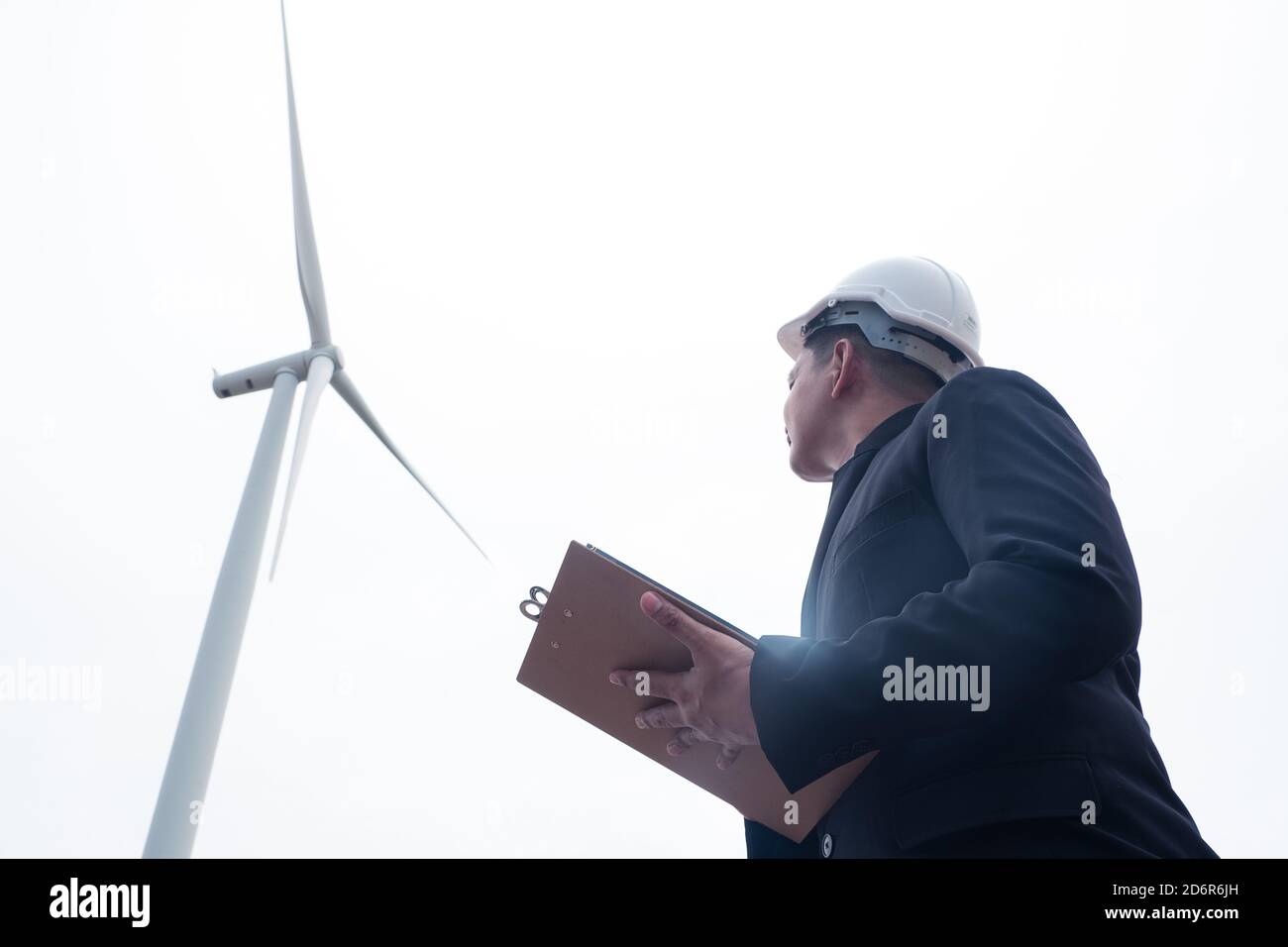 Male engineer looking and writing plan on clipboard against wind turbine Stock Photo