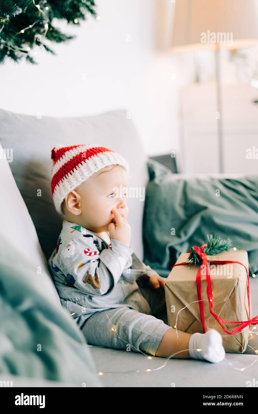 brooding little boy sits in Santa hat and holiday costume on gray sofa ...