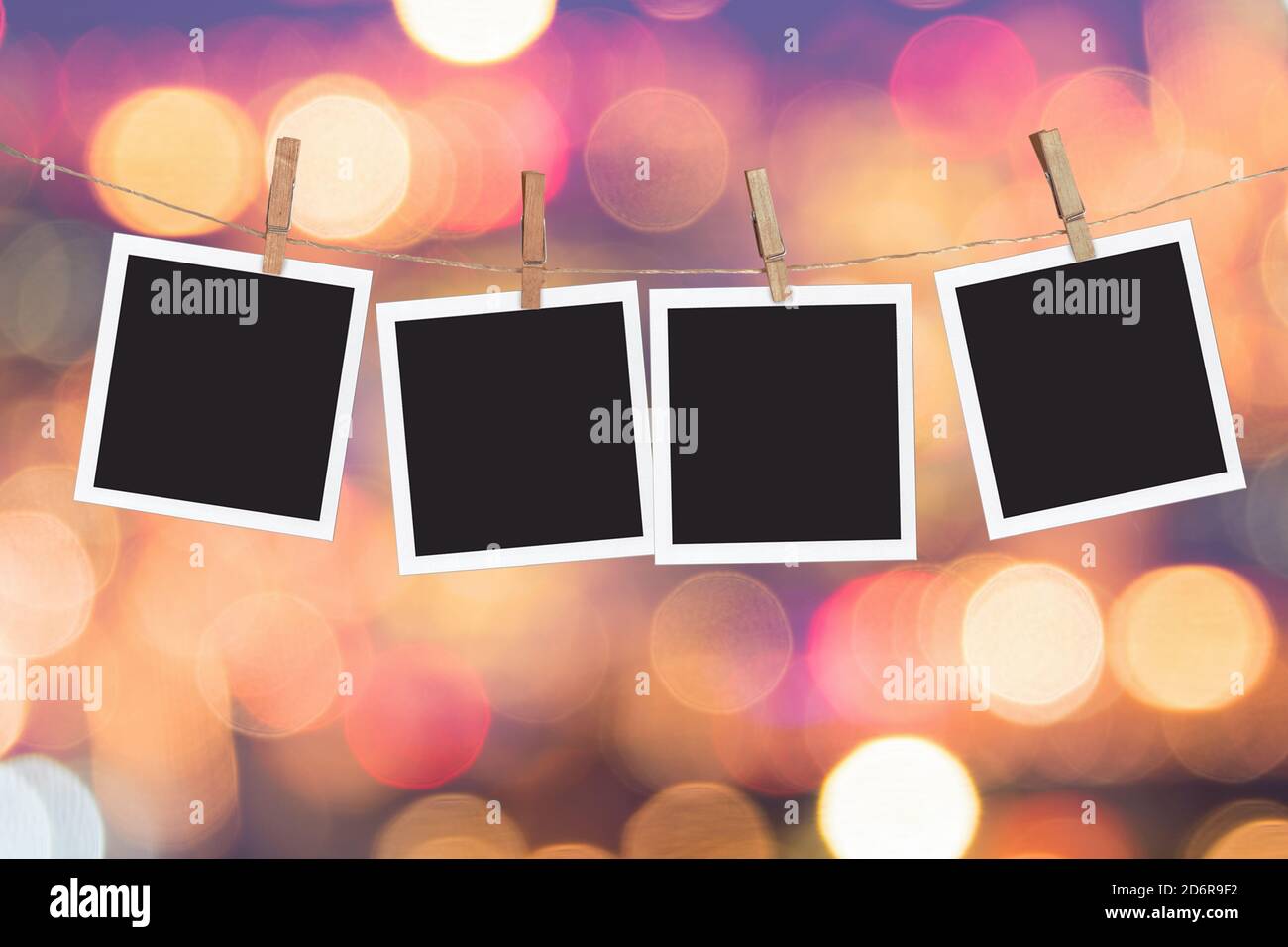 Four blank instant photo frames hanging on a rope, on holiday lights bokeh background Stock Photo