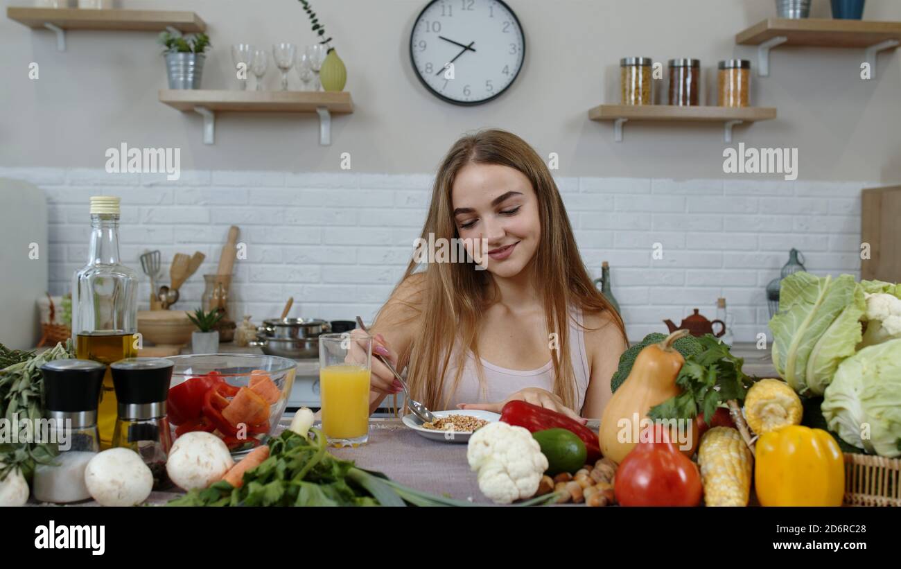 Lovely girl with long hair eating raw sprouts buckwheat with nuts in  kitchen with fresh vegetables and fruits. Healthy organic eco vegetarian  food concept. Weight loss and diet lifestyle Stock Photo -