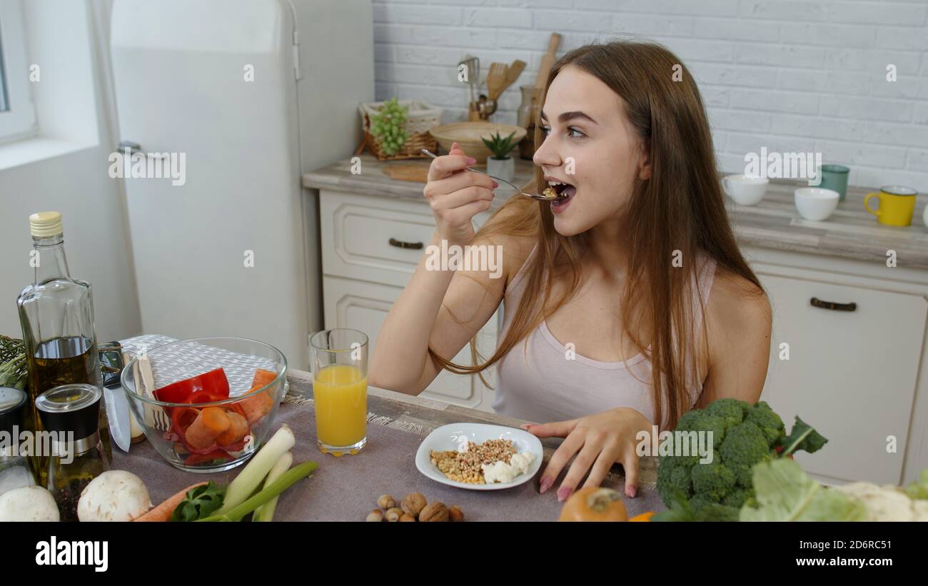 Lovely girl with long hair eating raw sprouts buckwheat with nuts in kitchen with fresh vegetables and fruits. Healthy organic eco vegetarian food concept. Weight loss and diet lifestyle Stock Photo - Lovely girl with long hair eating raw sprouts buckwheat with nuts in kitchen with fresh vegetables and fruits. Healthy organic eco vegetarian food concept. Weight loss and diet lifestyle Stock Photo -