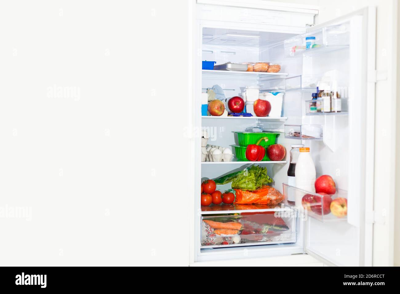 Top freezer kitchen refrigerator with doors open and shelves full of groceries with fresh and frozen food and cold bottles Stock Photo