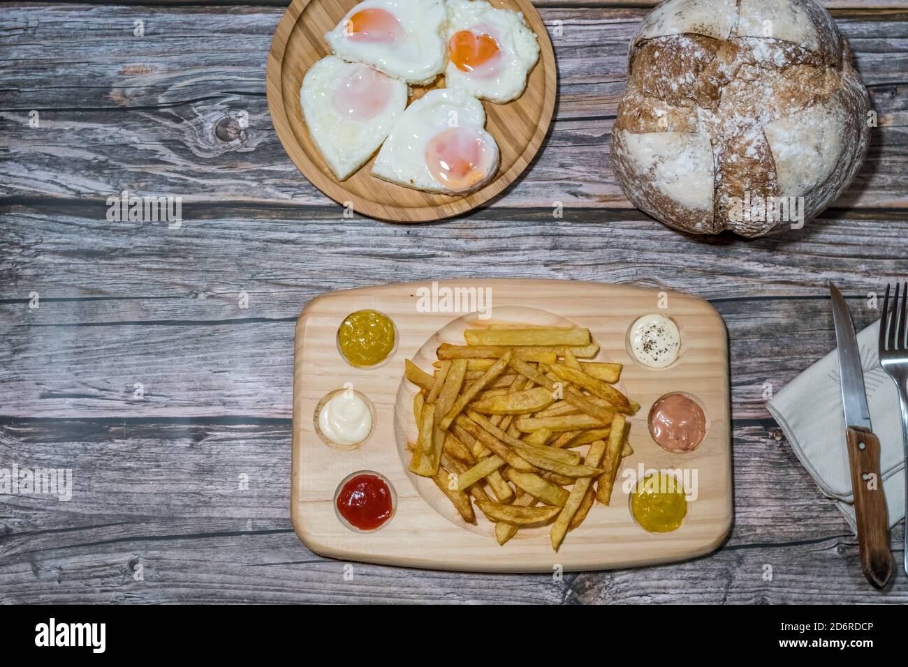 top view of a table of chips with various sauces, a table with fried eggs in the shape of a heart and a rustic village bread Stock Photo