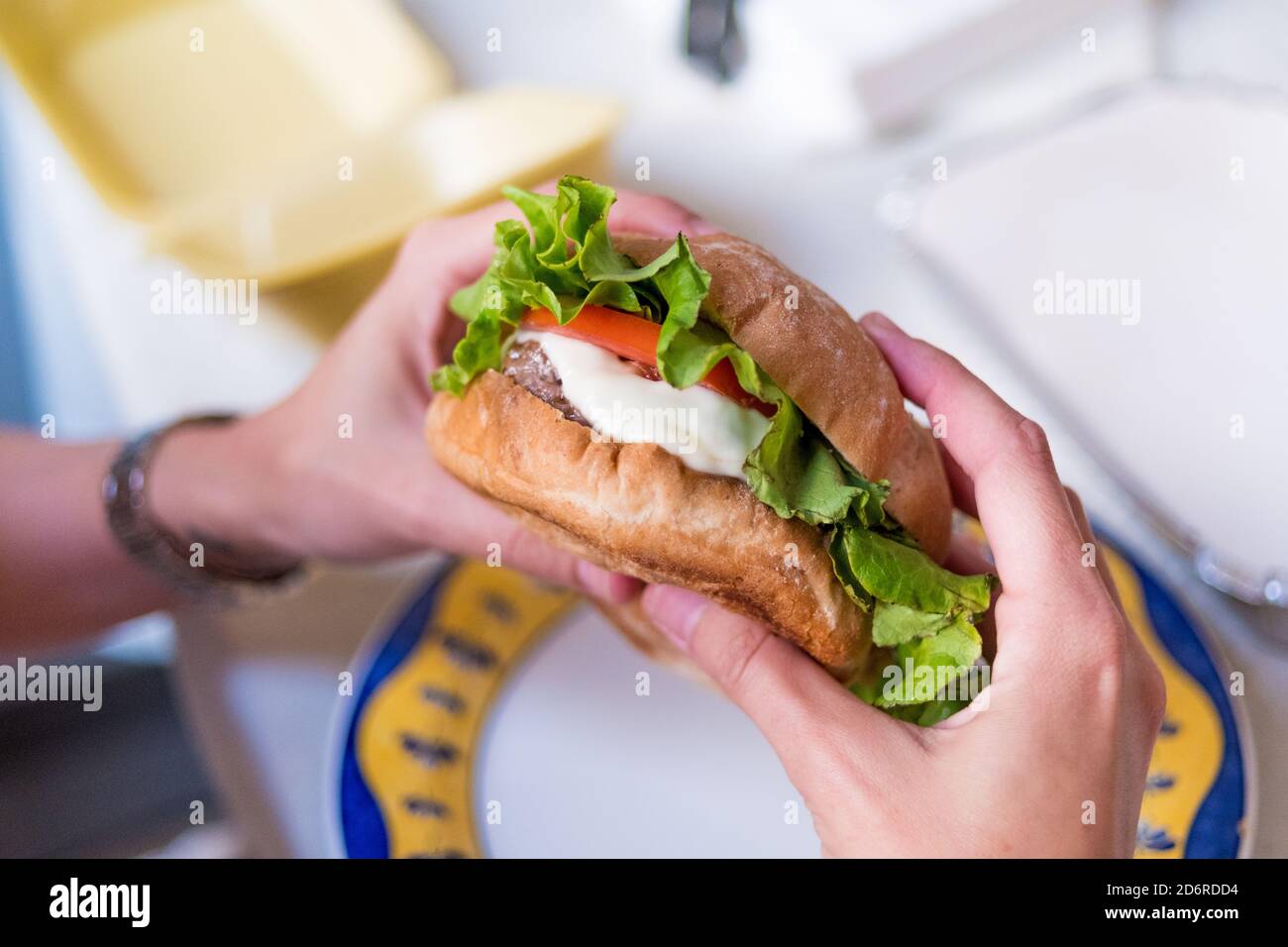 human hands holding a ready to eat cheeseburger with lettuce and tomato Stock Photo