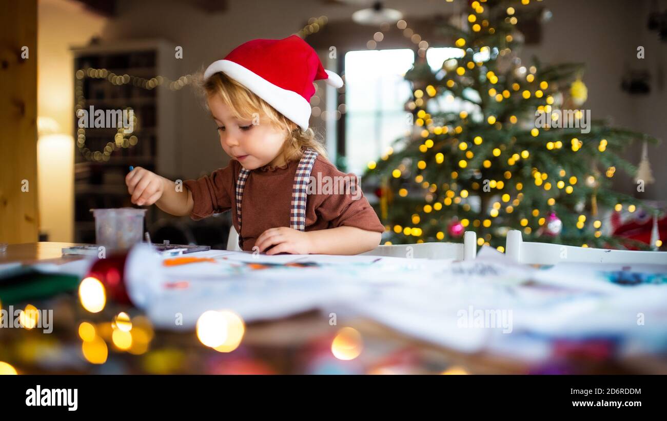 Portrait of small girl indoors at home at Christmas, painting pictures. Stock Photo