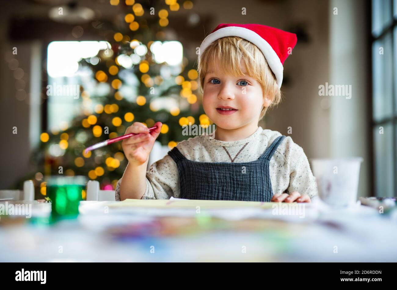 Portrait of small boy indoors at home at Christmas, painting pictures. Stock Photo