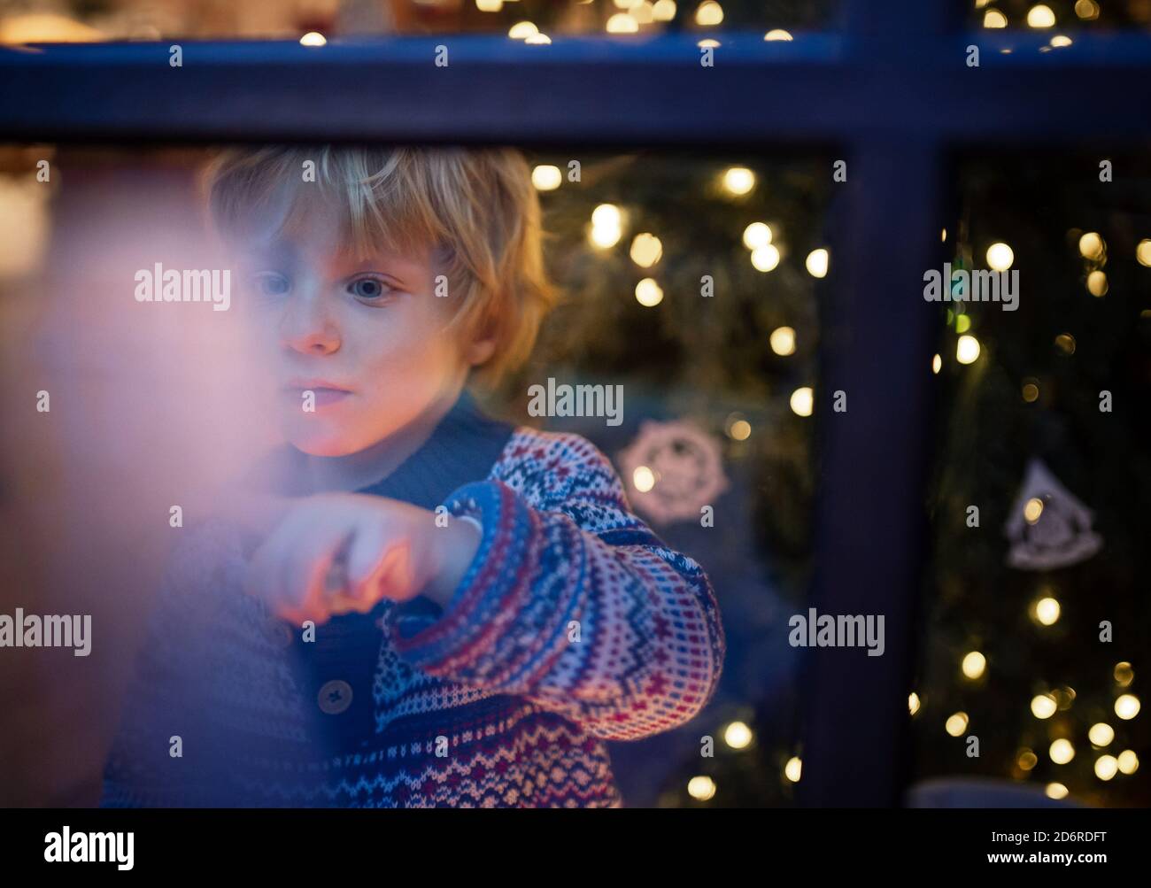 Portrait of small boy indoors at home at Christmas, playing by window at night. Stock Photo