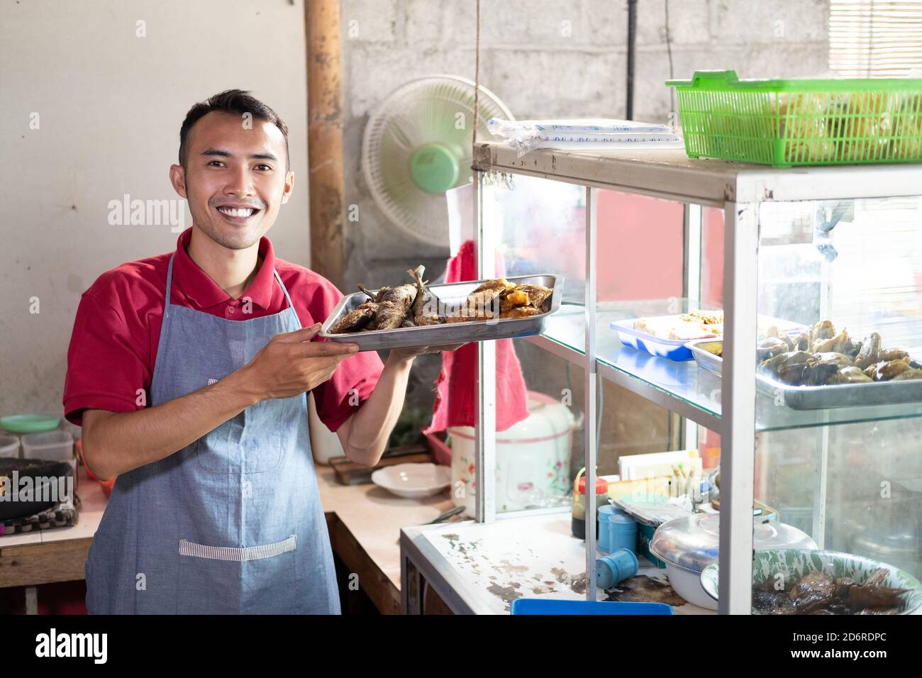 smiling male waiters carrying trays of side dishes near the display windows in food stalls Stock Photo