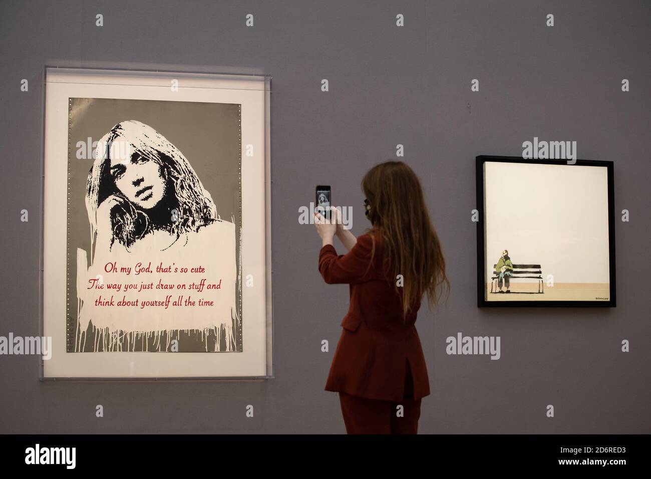 A gallery assistant takes a picture next to Oh My God 2006 by BANKSY (L) with a guide price of £700,000 to £1,000,000 and Weston Super Mare 1999 by BANKSY (R) with a guide price of £400,000-£600,000 at Bonhams in central London ahead of the auction house's forthcoming Post-War and Contemporary Art sale on October 22. Stock Photo
